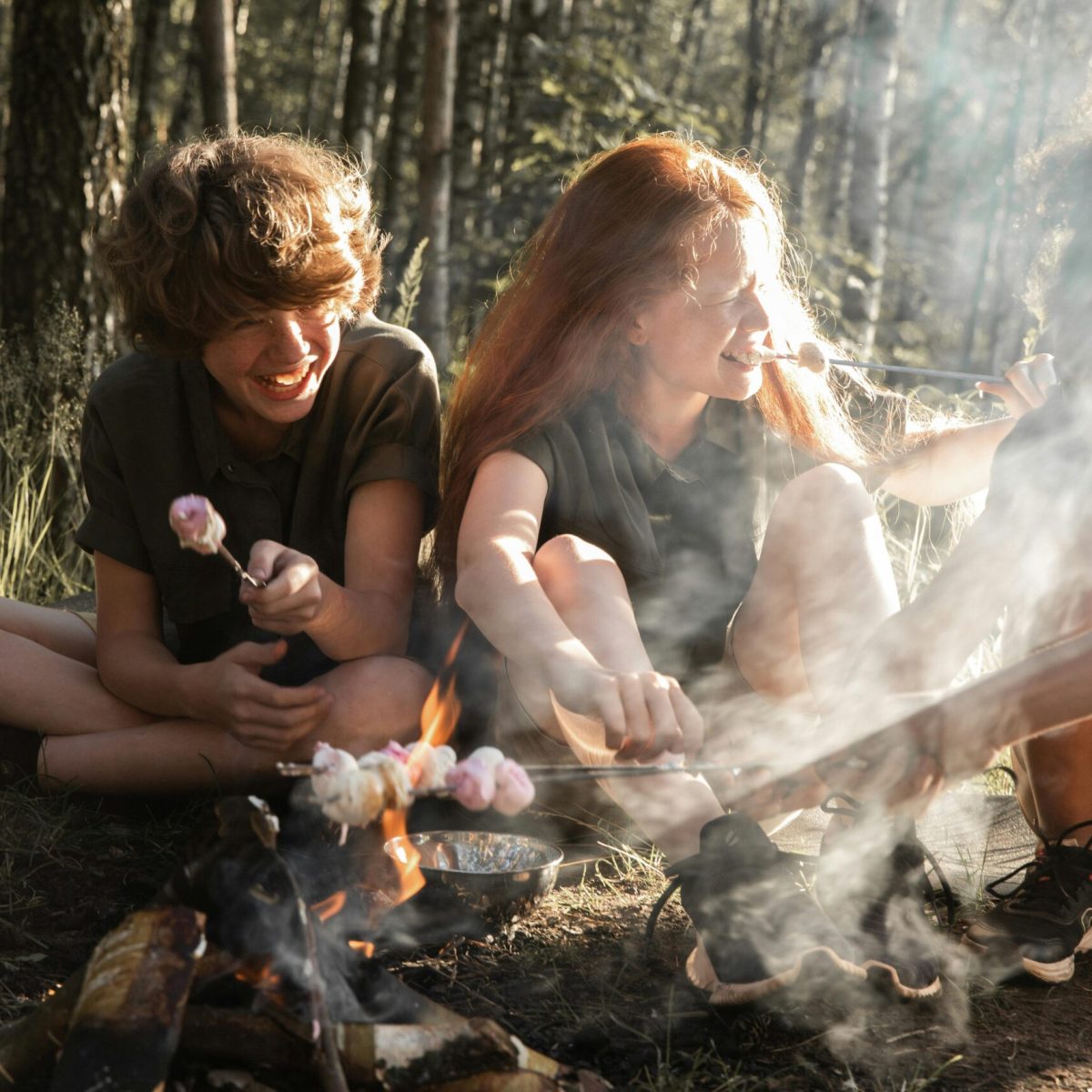 Group of teens roasting marshmallows around a campfire in the woods, enjoying nature.